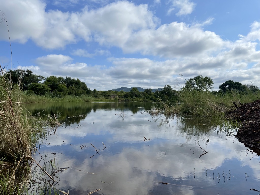 Calm lake reflecting clouds and bushland at Malinga Rise, Filabusi